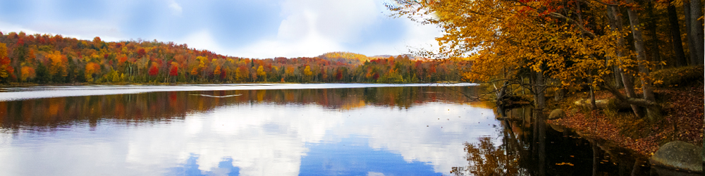 Image of the river and a mountain the back. The image is of crystal clear blue water, with beautiful orange, red and green trees surrounding the banks and mountains.