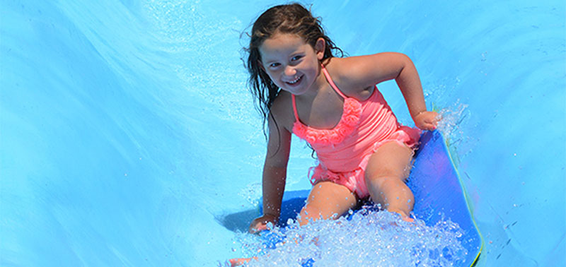 Image of a little girl in a pink bathing suit as she sits on a mat and goes down the pygmy slides