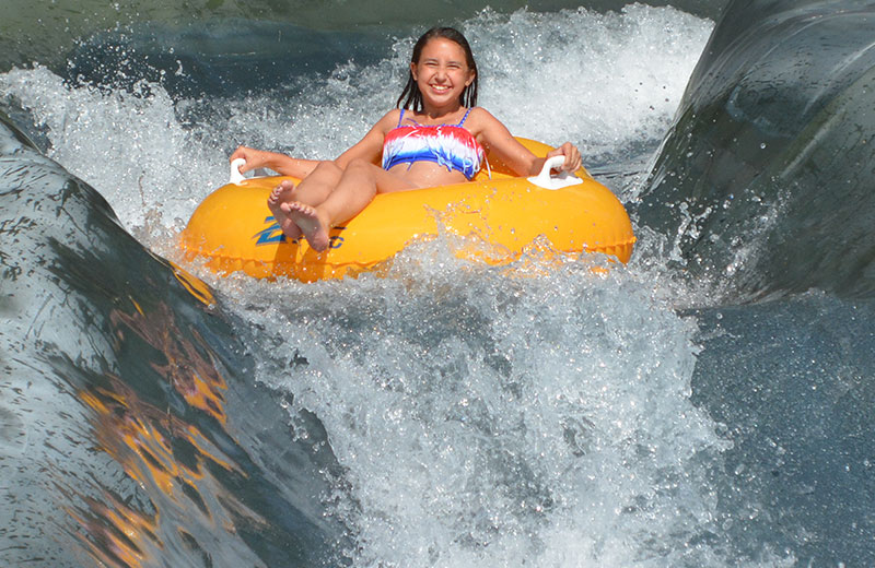 Image of a girl smiling while going down the raging rapids on a yellow tube.