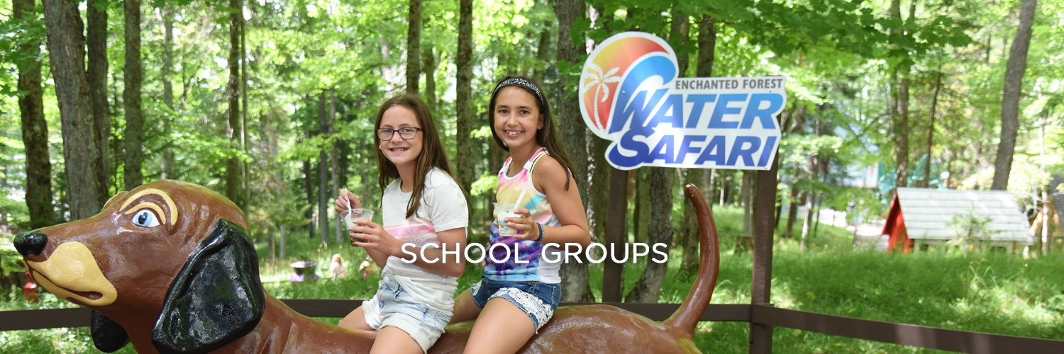 An image of two young girls holding Dippin' Dots and sitting on a large brown statue of a dog. Behind them are green trees and a pole with the Enchanted Forest Water Safari logo on it.