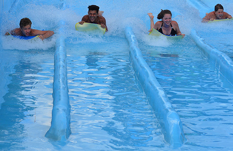 Image of four people sliding down the water slides face first on a mat.