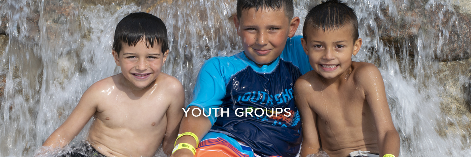 An image of three young boys in bathing suits smiling as water splashes behind them. There is white text centered at the bottom of the image that reads "Youth Groups".