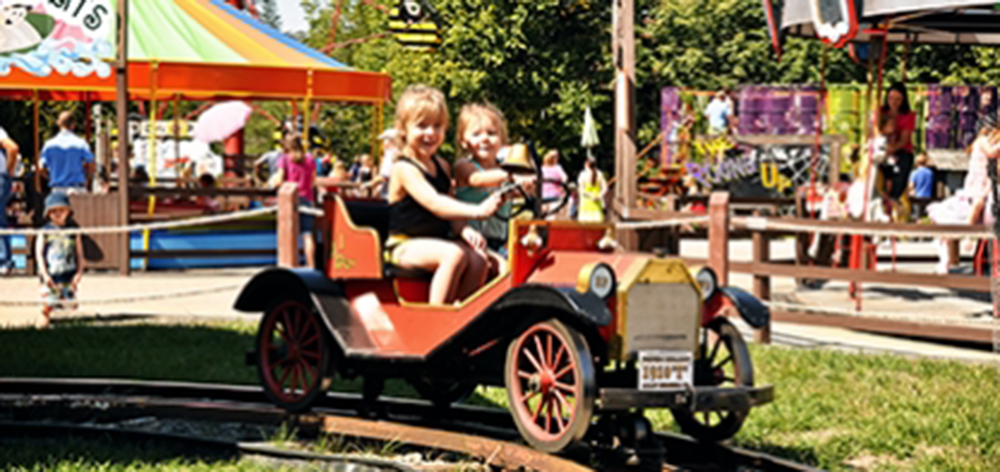 Image of two young girls smiling as they sit in the fiver car as they go around the track.