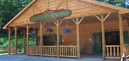 Photo of the log cabin Enchanted Memories Museum. The museum has a porch with purple hanging flowers and green doors leading inside.