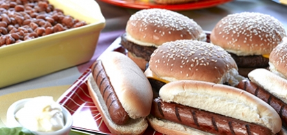 An image of flame-grilled hamburgers and hot dogs in buns.