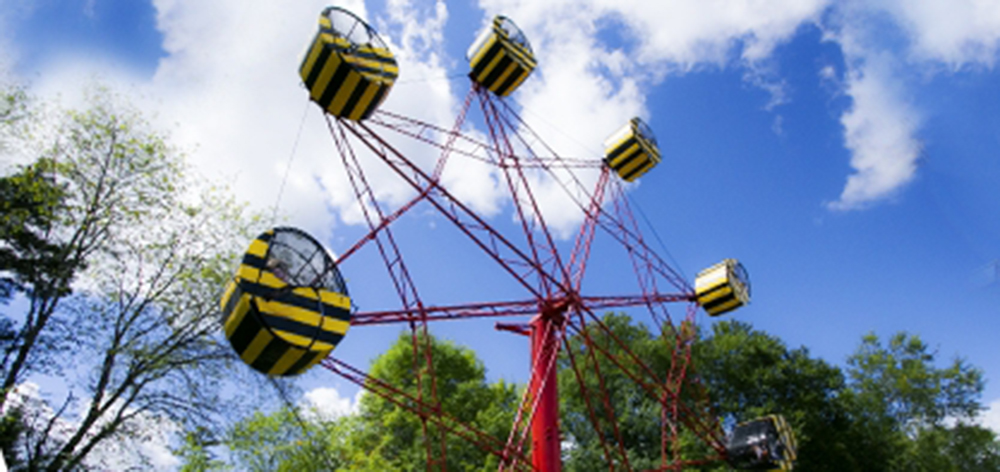 Image of the Rock-o-planes. The ride is pictured infant of the beautiful blue sky and trees behind it. The ride is a big rotation circle with comfortable cages for the guests to go in while the ride goes up and down.