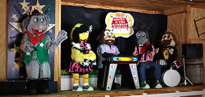 Image of the Rocky & the Ramblin' Rascals. A performing band, the band is centerstage. The characters look like puppet animals. there is a cow, donkey and bird