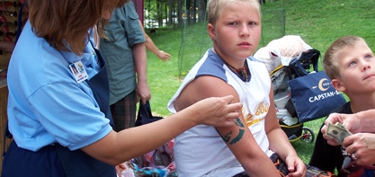 Image of a young boy who is getting anatto put on by an employee on his upper arm.