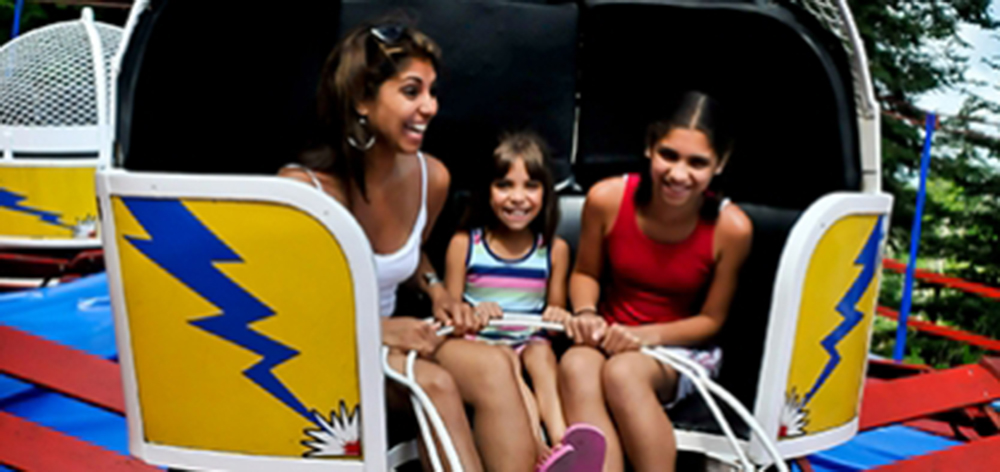 Image of a mother and her two daughters smiling as they ride the tilt-o-whirl.