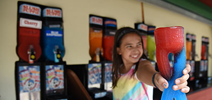 Image of a girl smiling and holding a slushy out to the camera