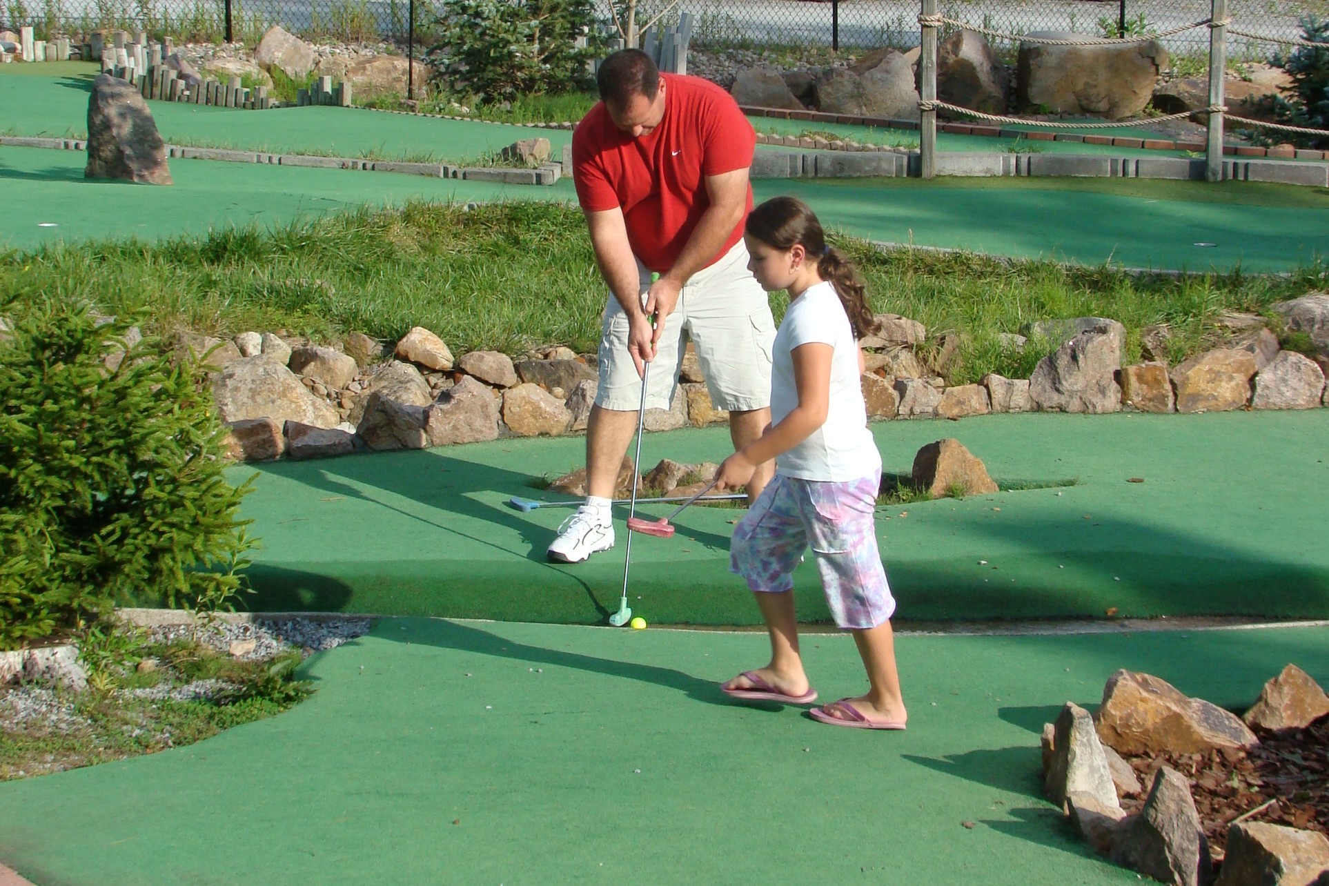 Image of a man and young girl playing Calypsos Cove Mini Golf on a lovely day