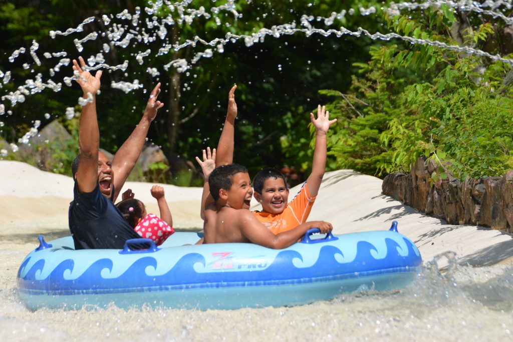 A family getting sprayed with water on the Amazon ride. Their hands are up and all four of them are laughing and smiling