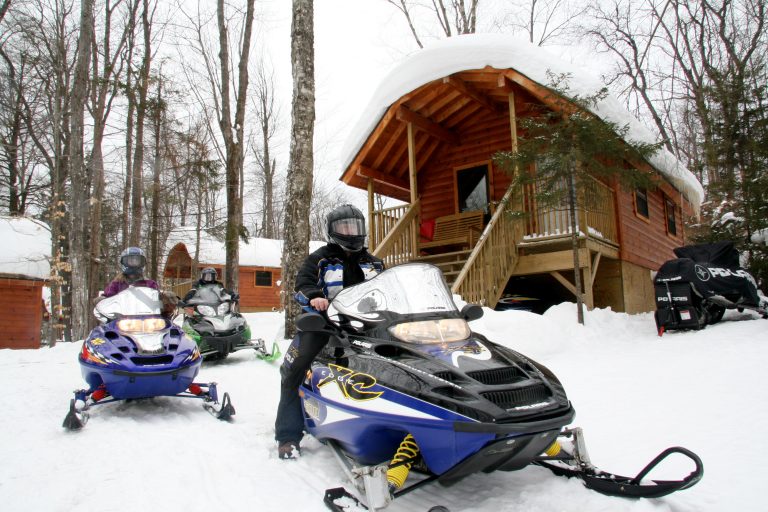 Photo of three snowmobile riders starting to ride out into the snow with the camping resort cottages in the background.
