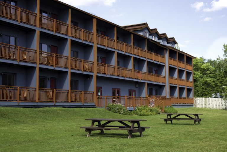 Image of the Waters Edge Inn exterior. There are two picnic tables outside with green grass and sunny skies.