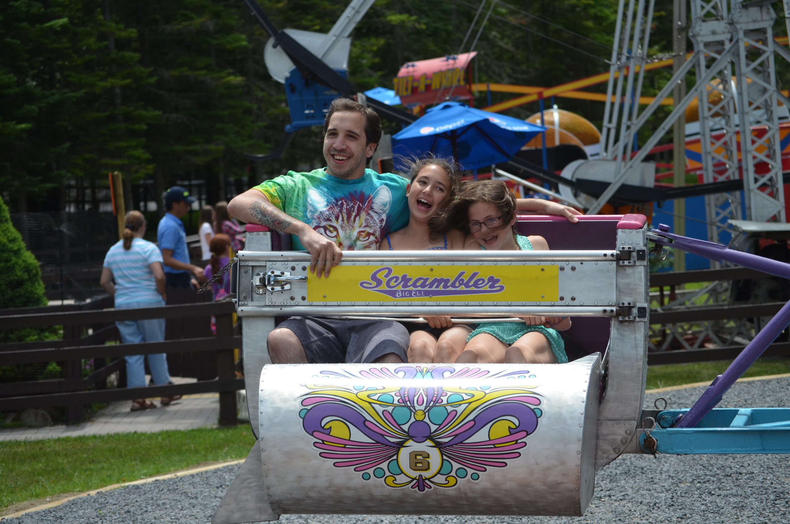 An image of three people, a man and two young girls, laughing and smiling as the ride the Scrambler.