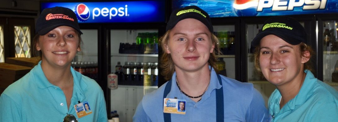 Image of three staff members smiling at the camera. they are in blue polo shirts and water safari hats. They are inside a restaurant.