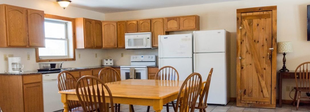 Image of the kitchen in the vacation house. The appliances are all white with tiled floor. Theres a large kitchen table in the kitchen that can seat 6