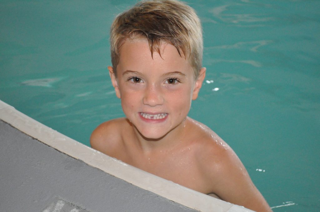 An image of a young boy smiling in a pool.