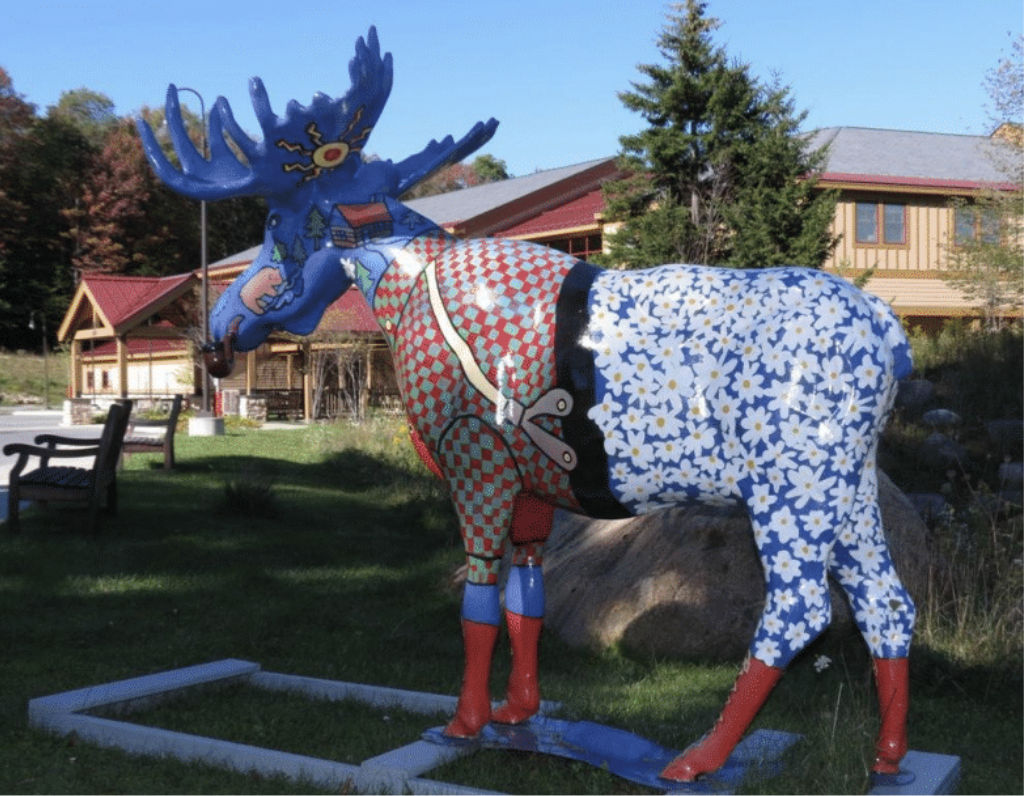 A statue of a moose that has many different patterns all over its body and the View Art center is in the background